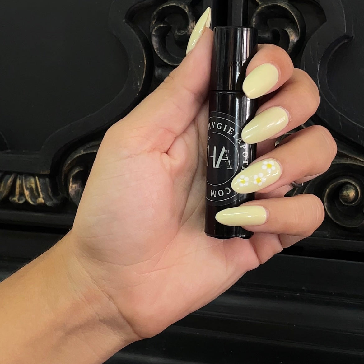 Female hand with pastel yellow gel nails holding a black roller bottle with the logo of Hygieia Apoteca