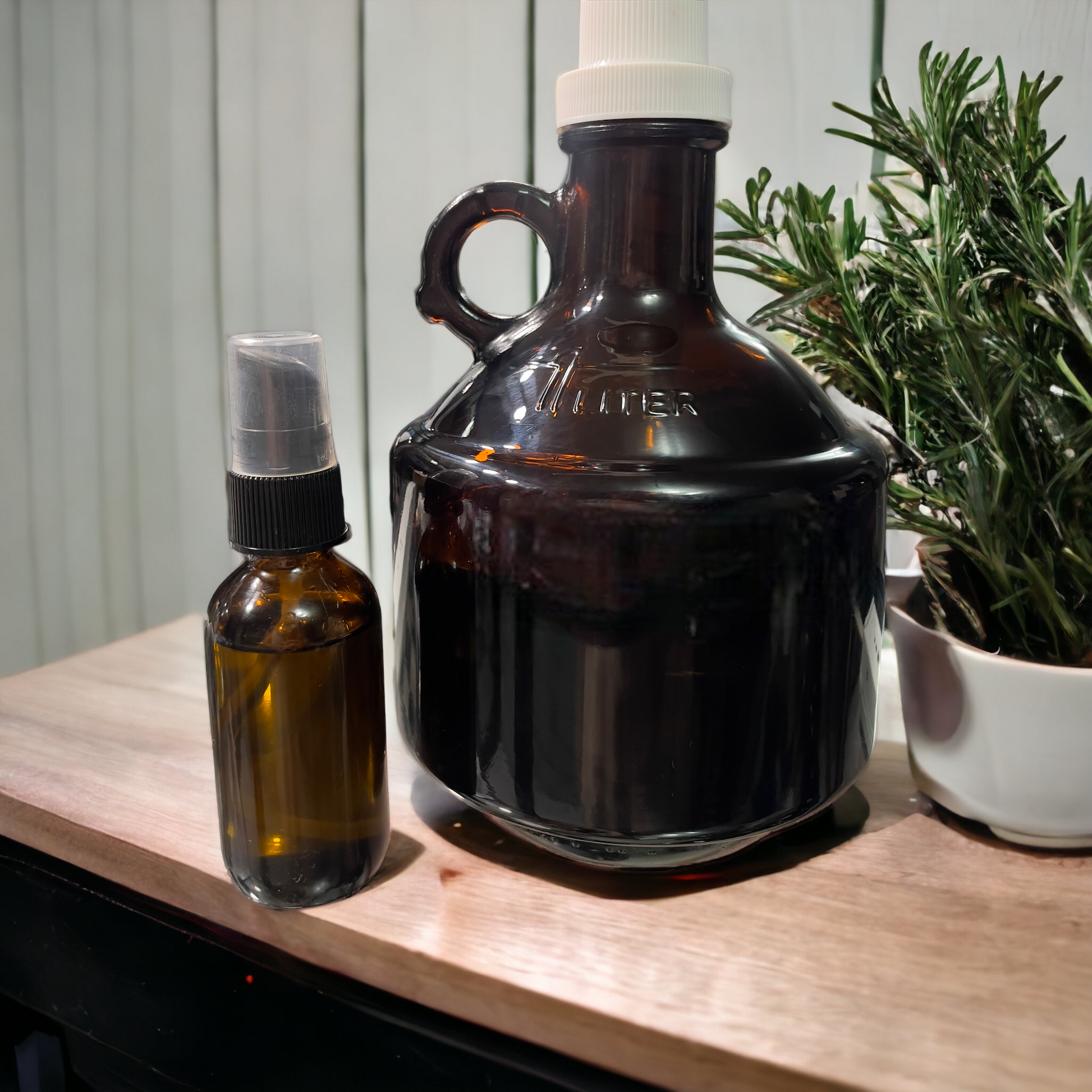 an amber glass jug and an amber 1.8 ounces glass bottle of beard oil on a wood counter next to a rosemary plant